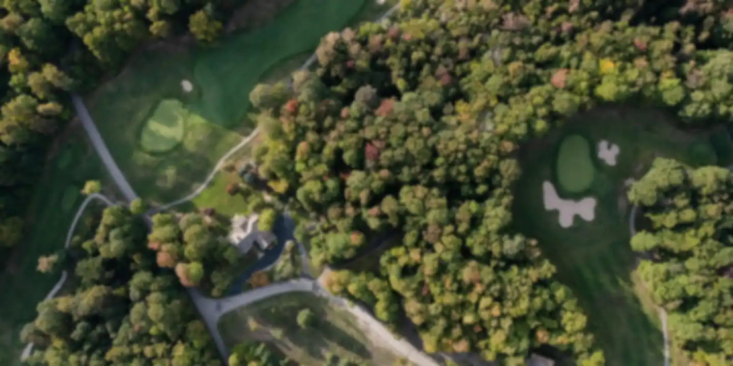 Aerial view of two golf holes separated by woodland