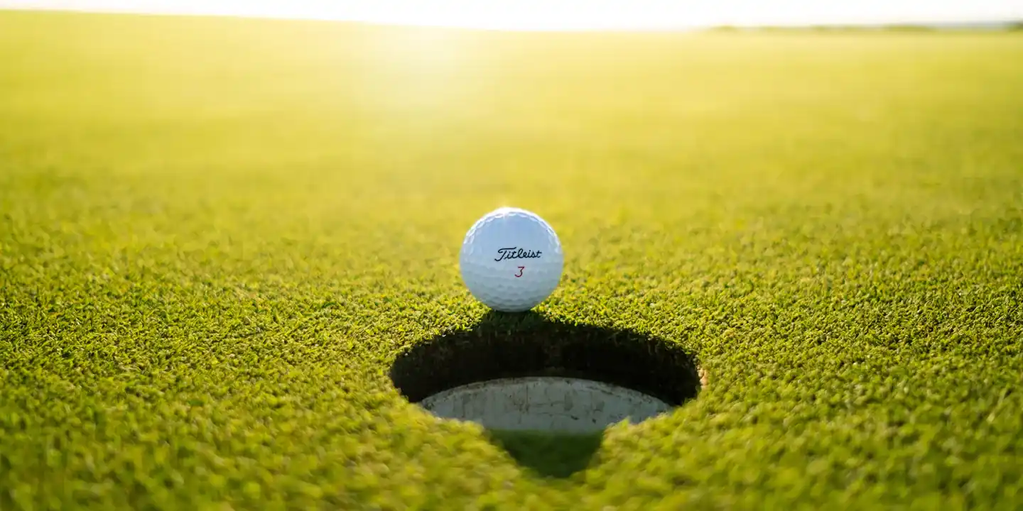 Golf ball sitting on the edge of the cup on a sunlit green