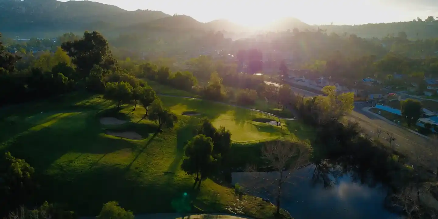 Aerial view of a golf course at sunset with the sun over the hills