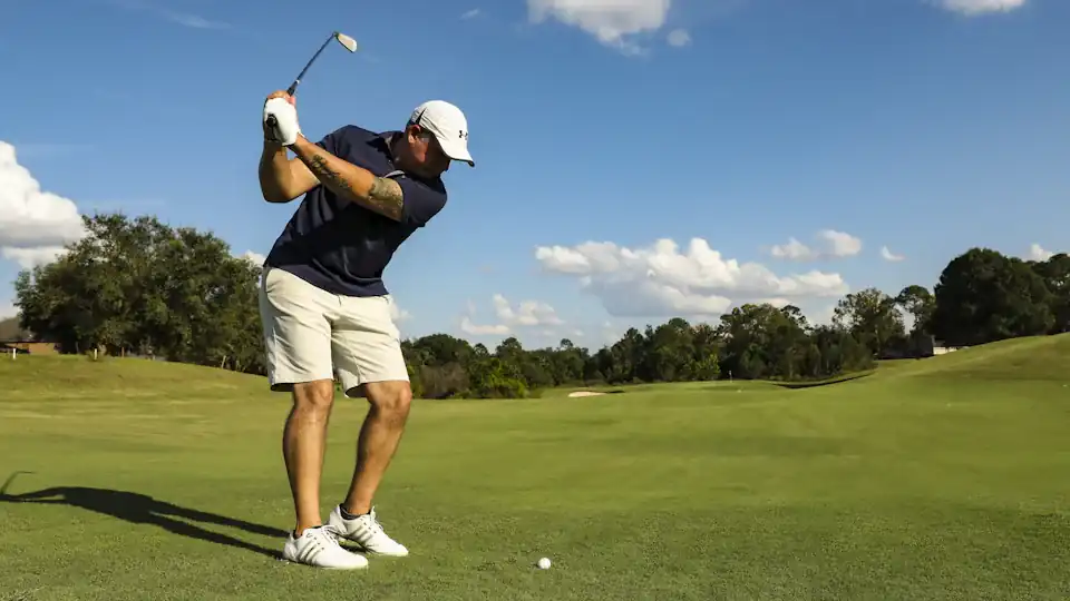 Golfer in a white cap swinging a driver under a blue sky