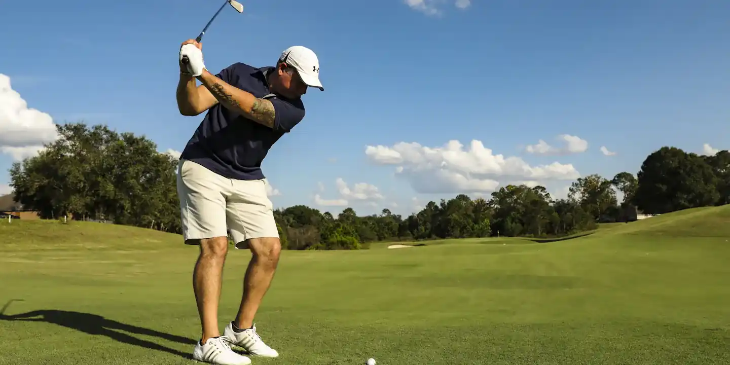 Golfer in a white cap and navy shirt swinging a driver