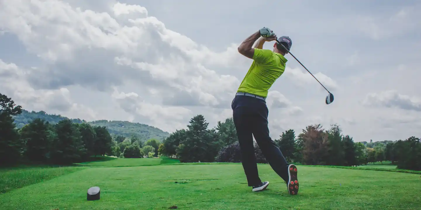 Golfer finishing a drive on a tree-lined tee box during a Wolf game