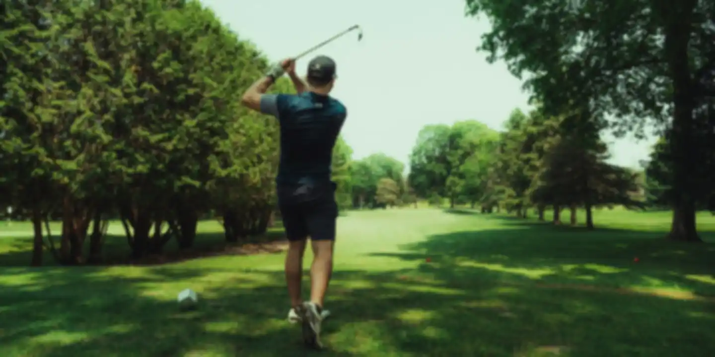 Golfer swinging on a fairway lined with tall trees