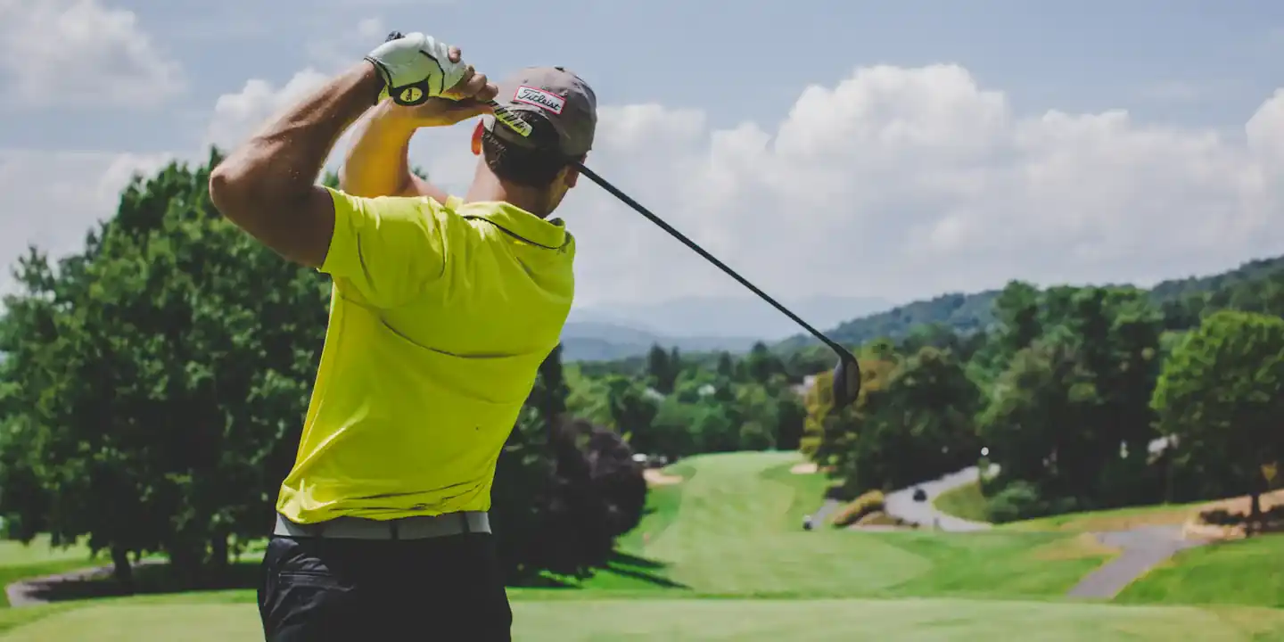 Golfer in a yellow shirt watching his drive from the tee
